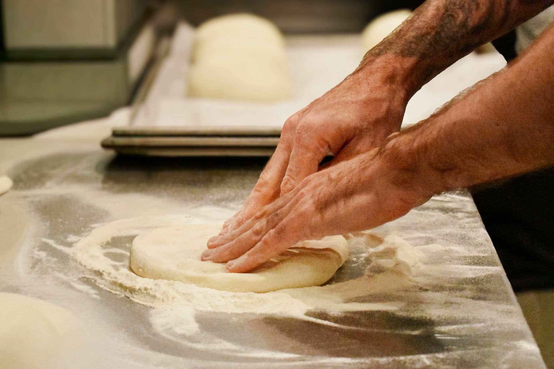 two hands push down on uncooked pizza dough
