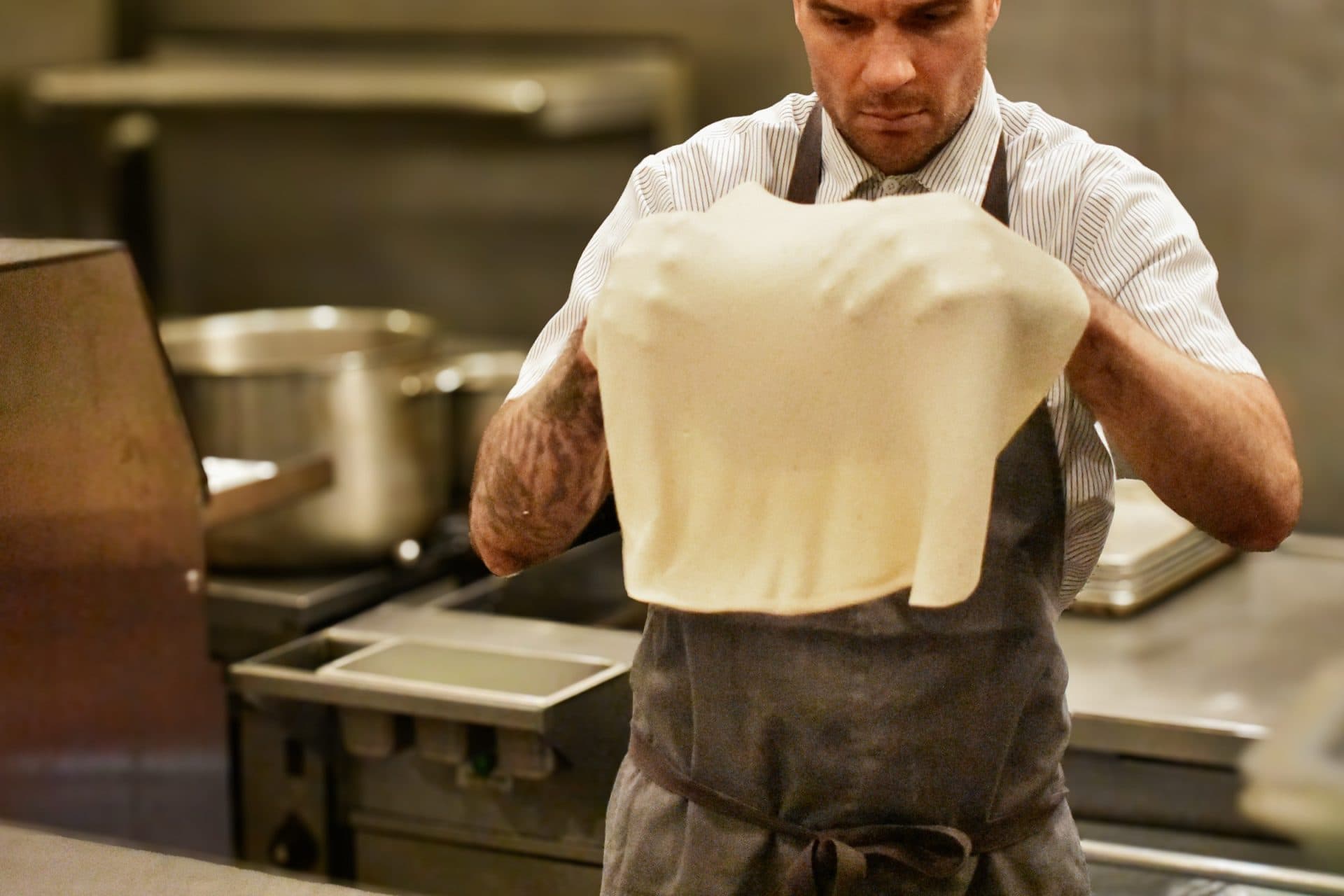 a chef holds up pizza dough which covers his hands