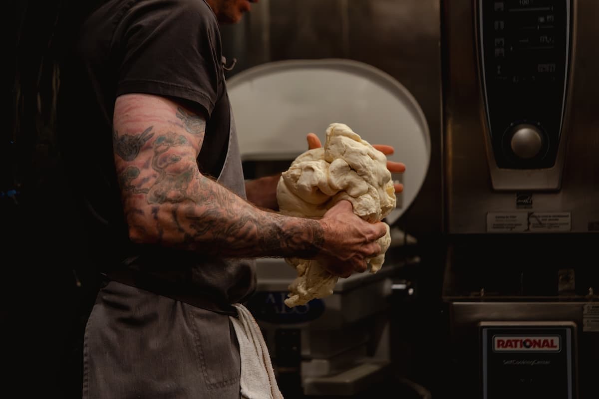 a man with a tattooed arm handles pizza dough