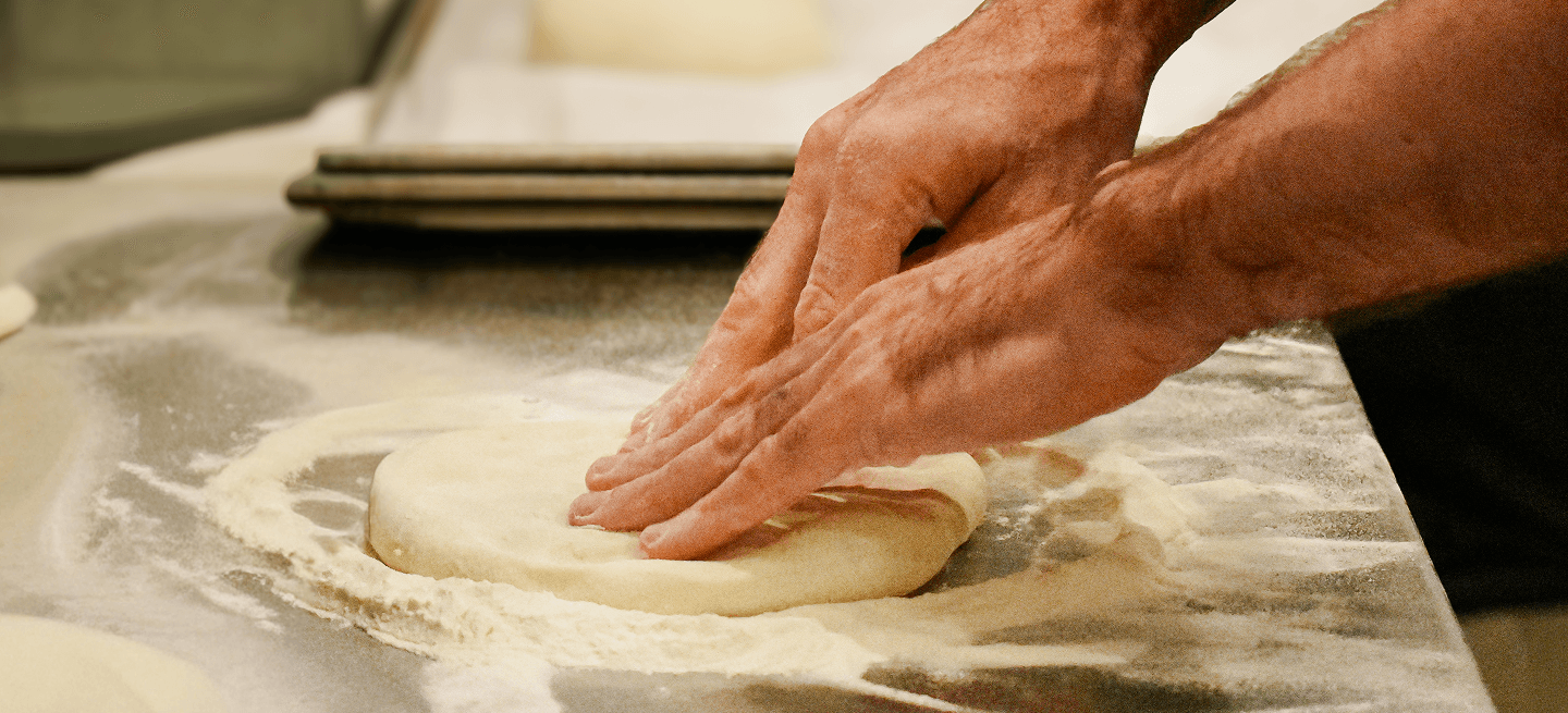 a chef covers uncooked bread with flour on a table with a wooden roller